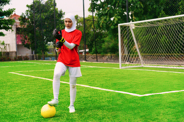 Top-Rated Goalkeeper Gloves for Serious Players 16 16 Confidence young female soccer goalkeeper wearing a white hijab and a red jersey is seen adjusting her black and yellow goalkeeper gloves with a focused yet cheerful